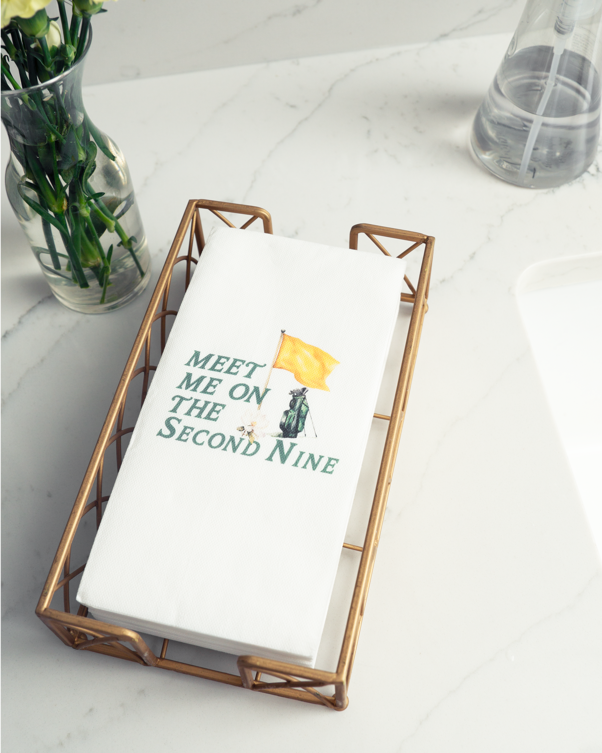 a white napkin with a humorous text printed on it, placed in a metal tray on a marble countertop.