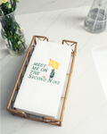 a white napkin with a humorous text printed on it, placed in a metal tray on a marble countertop.