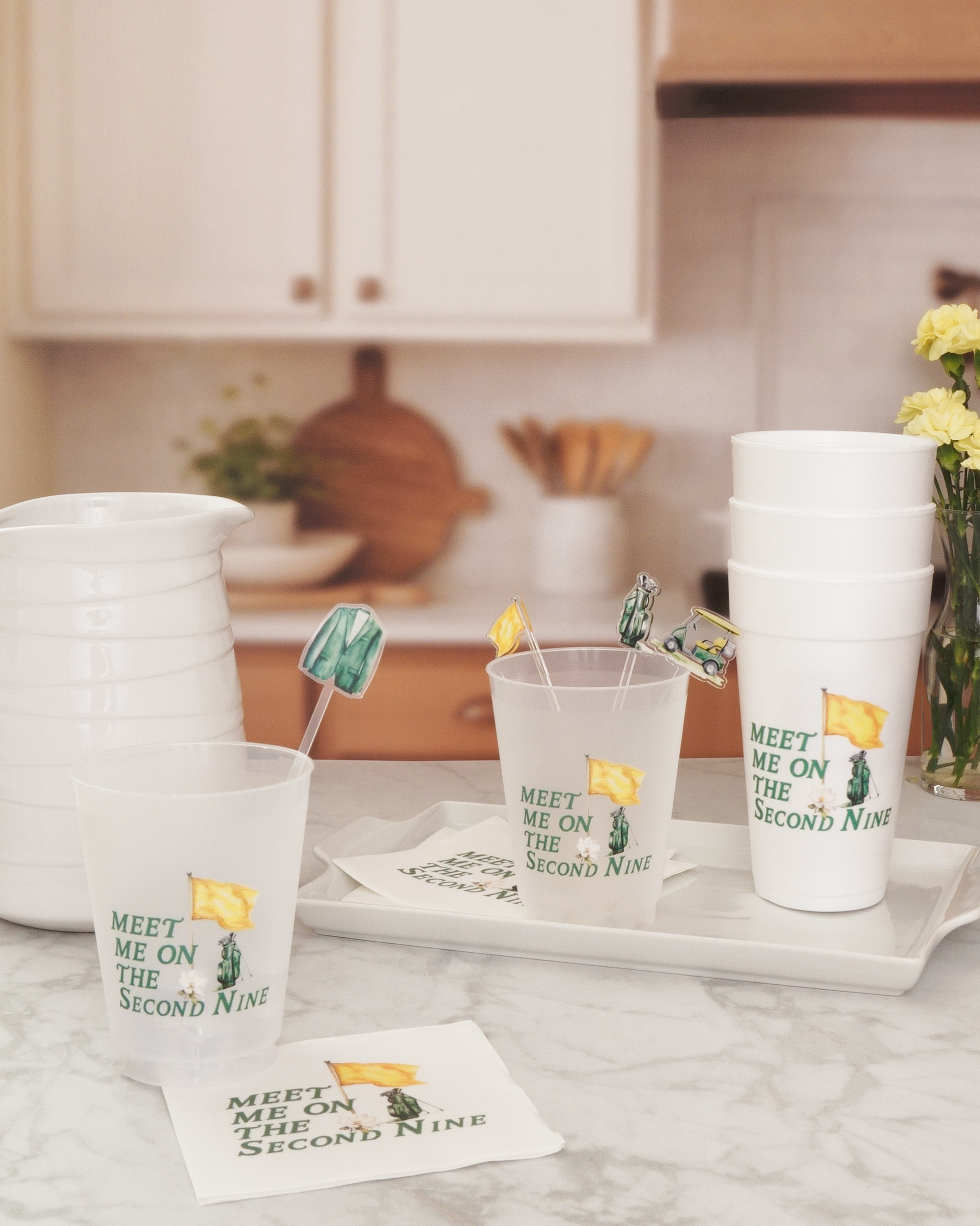 a kitchen counter with various items, including cups, a pitcher, and a vase with yellow flowers.
