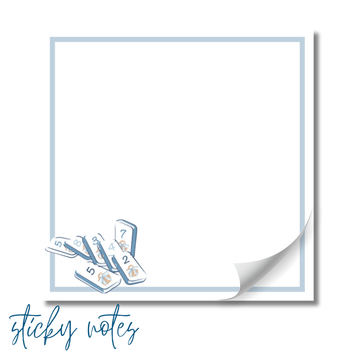 A blank white sticky note with a blue border, and a stack of dominoes with numbers on them.