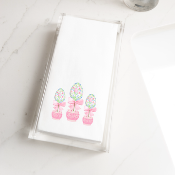 A clear napkin holder with a decorative Easter egg design on it, placed on a white marble countertop.
