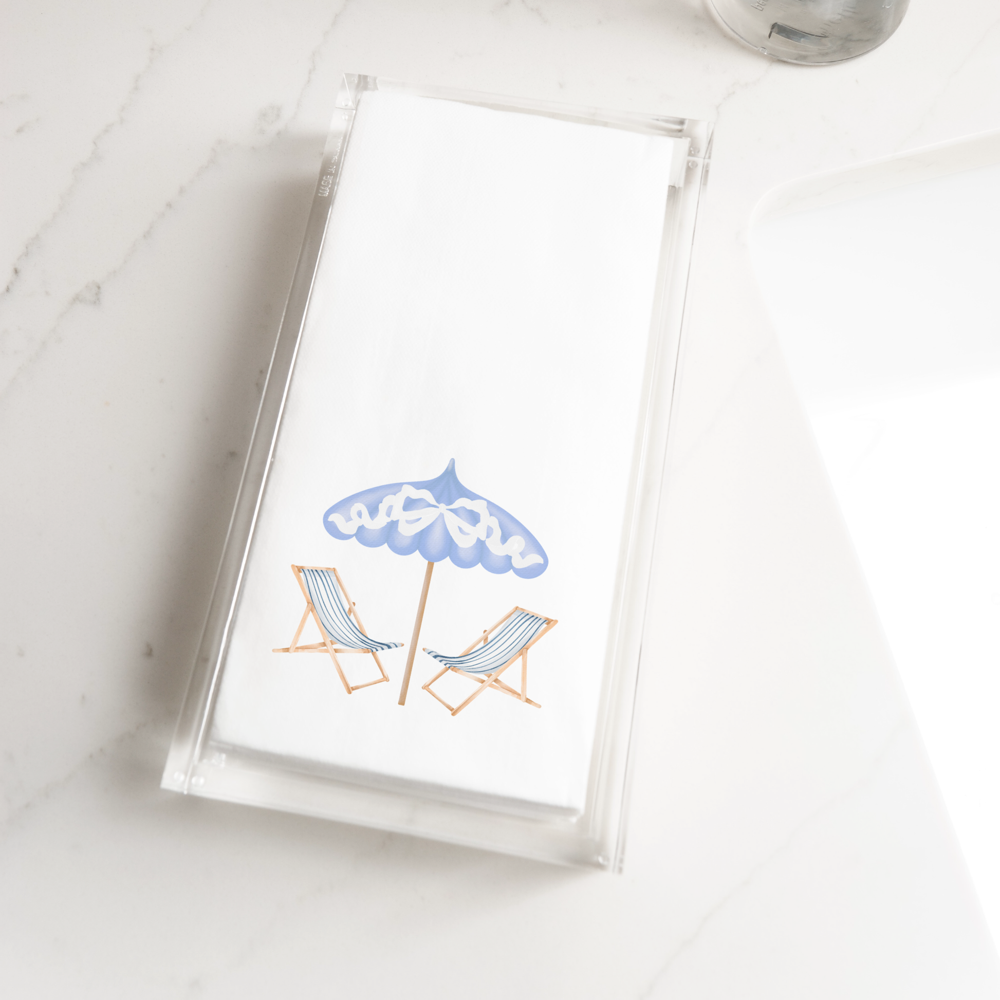 A clear plastic tray with a white napkin on it, featuring a blue umbrella and two lounge chairs.
